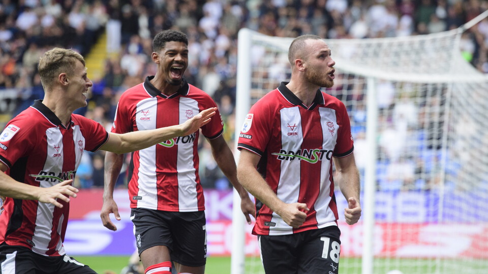 Football players in red and white striped shirts celebrate a goal