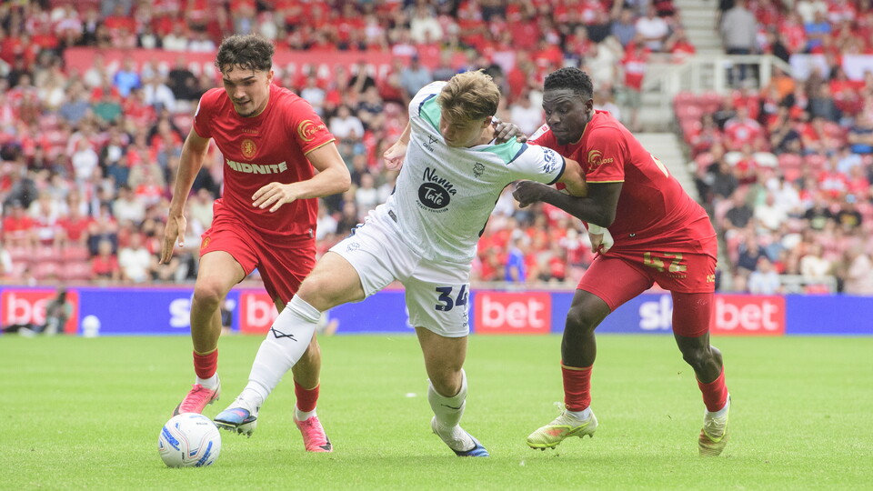 Two footballers in red shirts try to get the ball off one in a white shirt.