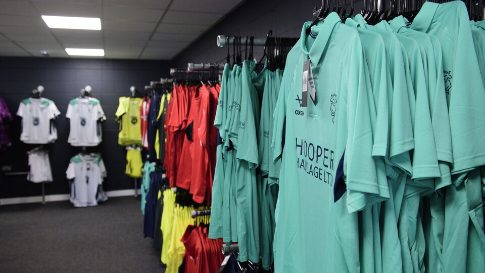 Green polo shirts hung up on clothing racks, with more t-shirts behind