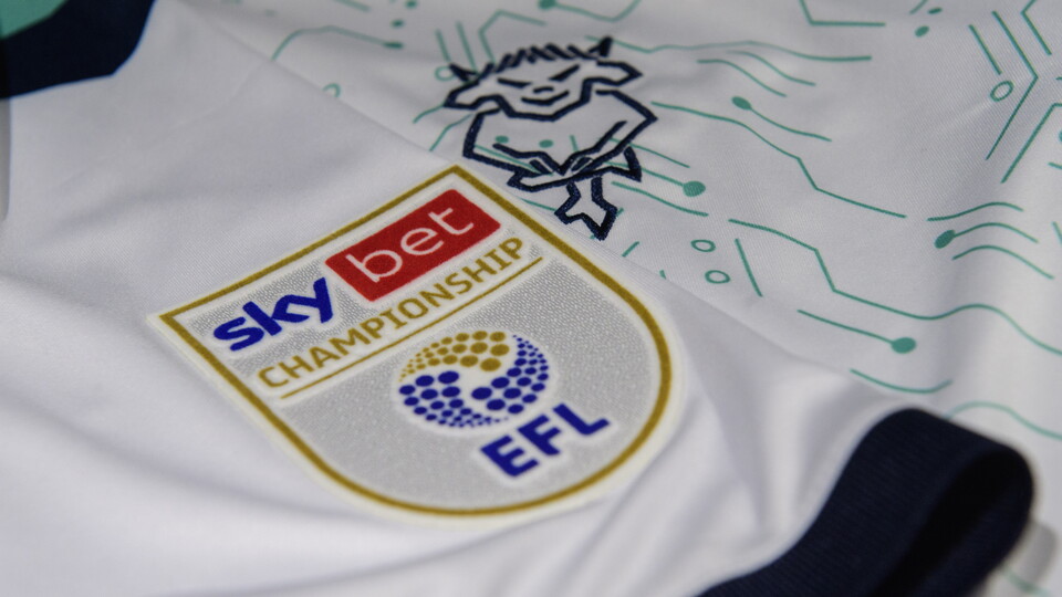 A close up of the Sky Bet Championship badge on a white Lincoln City third shirt.