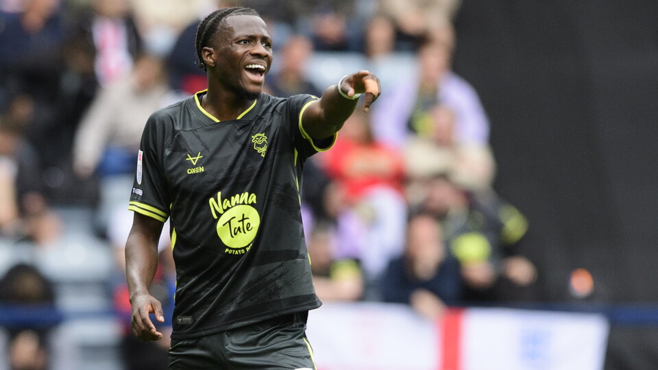 A man in a black football top points with his left hand and shouts in the same direction