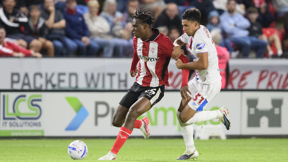 A man in red and white stripes shields a football from an opposition player in white