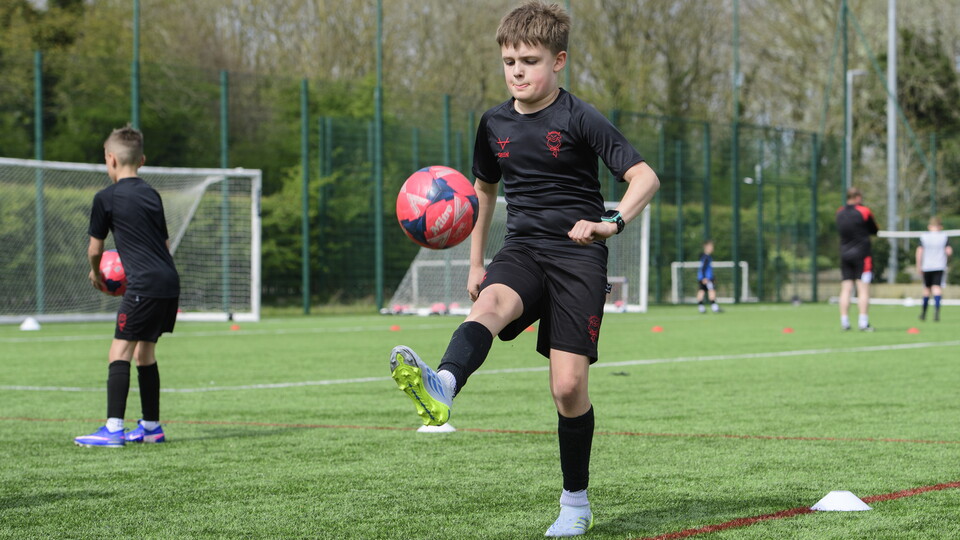 A boy wearing black t-shirt and shorts kicks a football