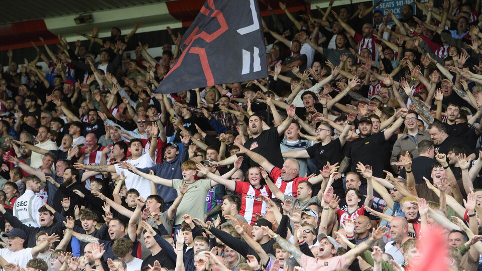 Lincoln City supporters hold their hands up in celebration in a packed stand